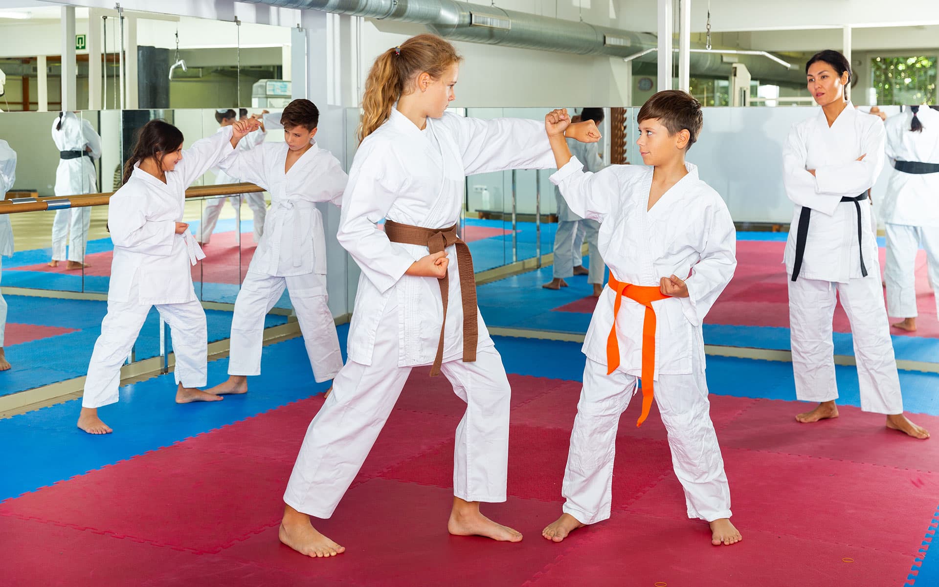 Young martial arts students practice karate techniques in a dojo while an instructor supervises, highlighting the need for dojo software to manage classes and student progress.
