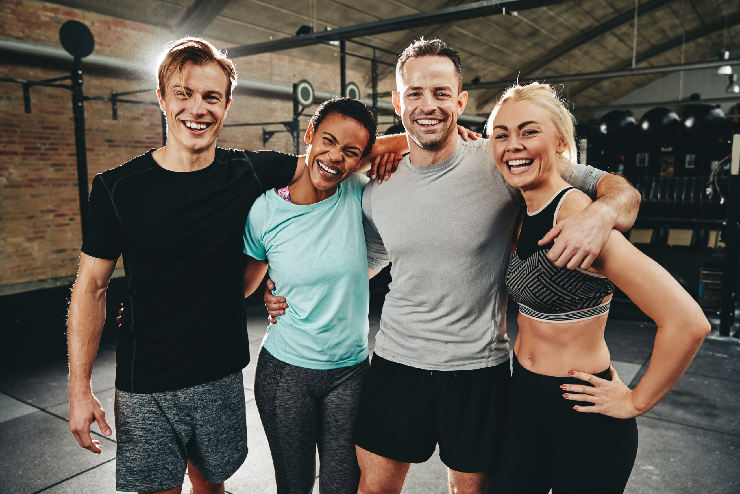 Diverse group of friends laughing and posing after a workout at the gym.