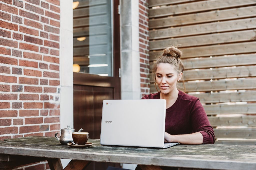 Woman with hair in bun using laptop next to brick wall