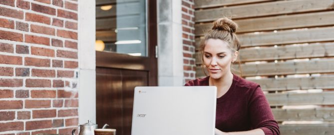 Woman with hair in bun using laptop next to brick wall