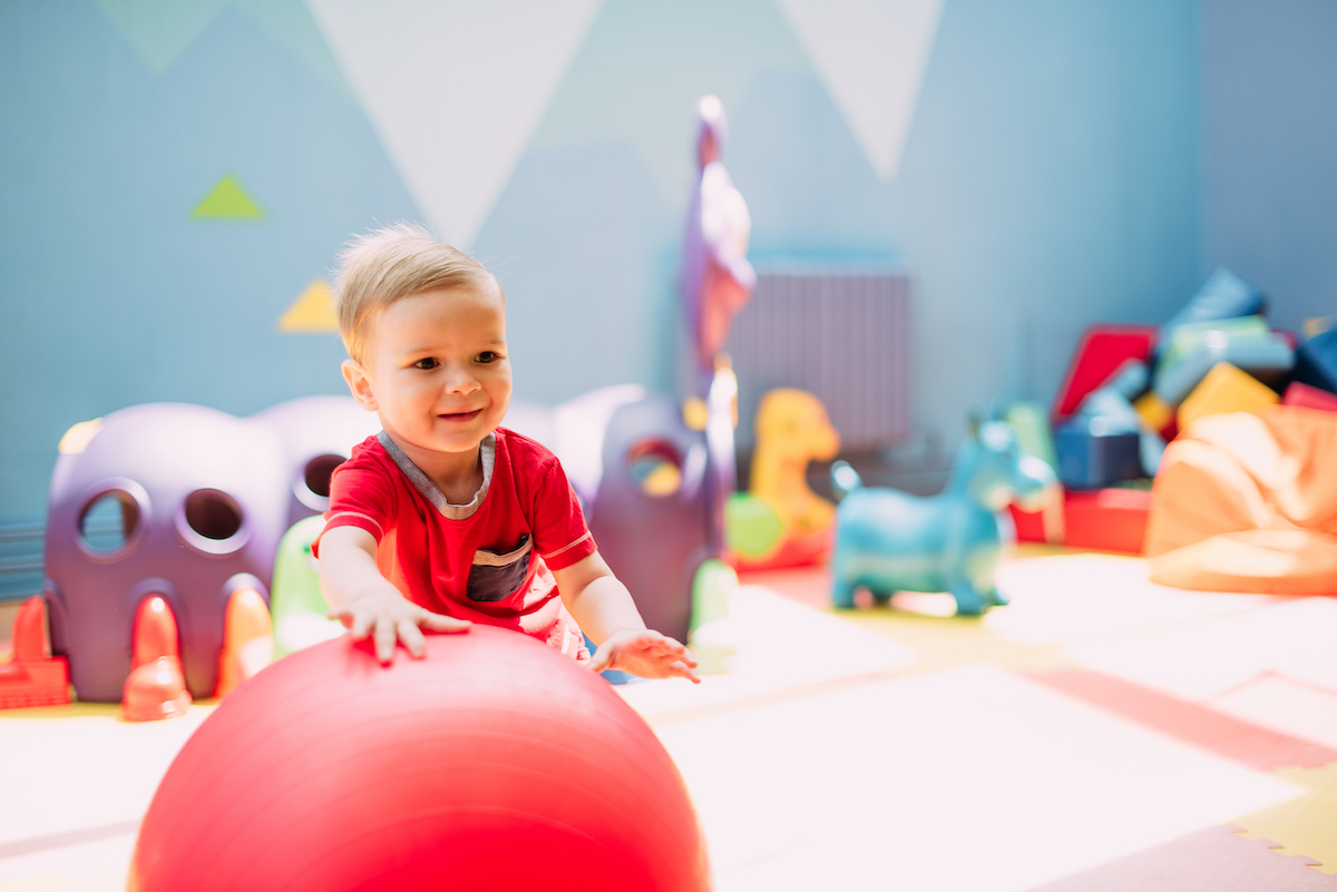 Toddler boy playing with red ball at gym daycare