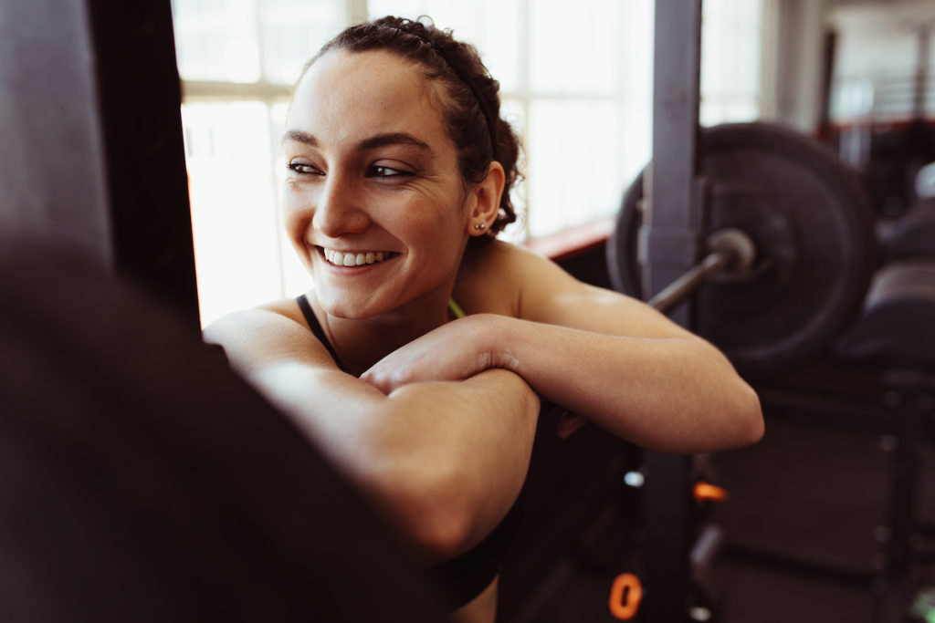 Woman resting on a barbell and smiling in the gym