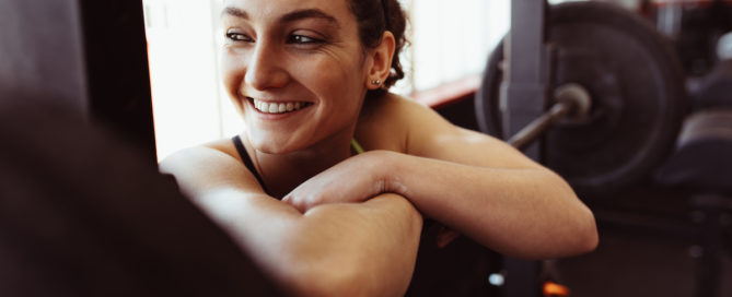 Woman resting on a barbell and smiling in the gym