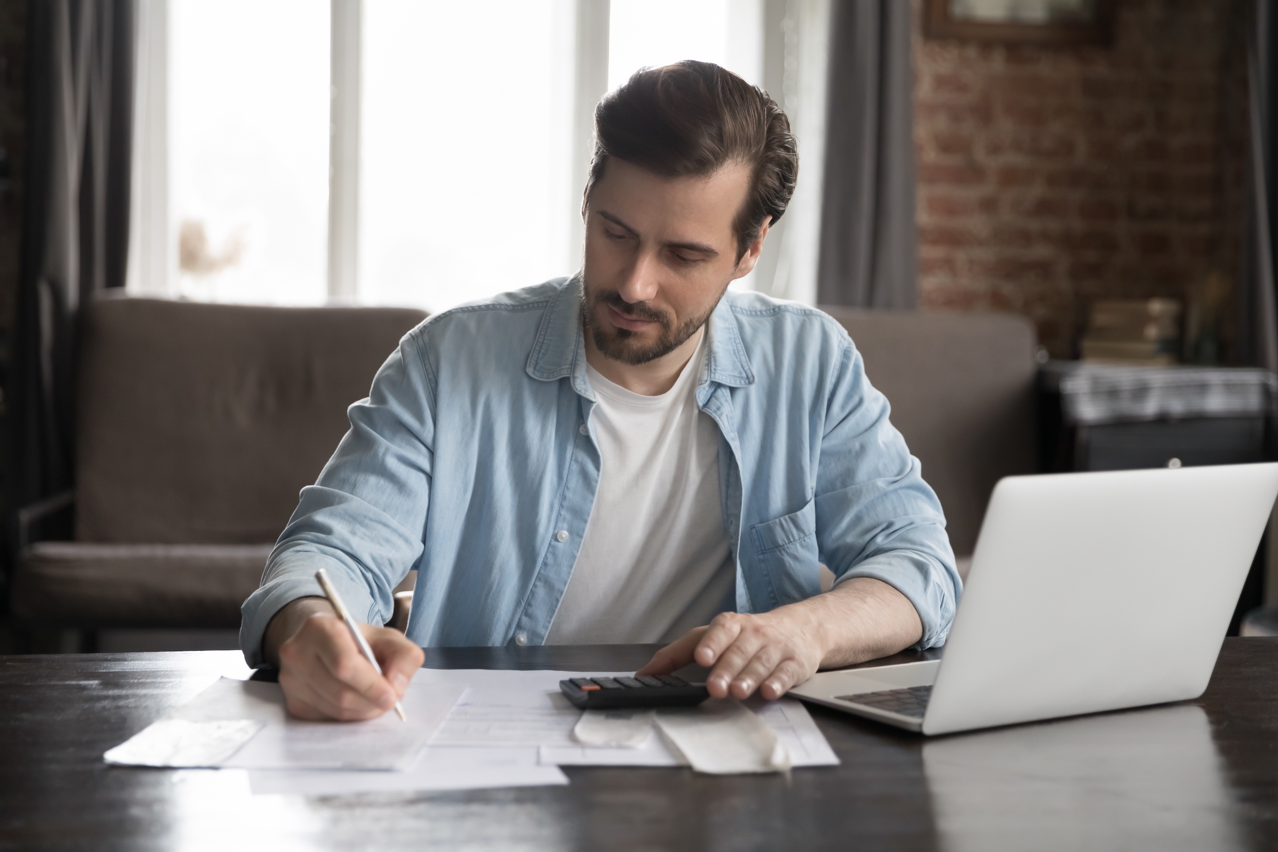 A man sitting and filing taxes for his small business using a laptop and calculator