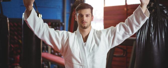 Martial artist in uniform raising hands confidently in a dojo.