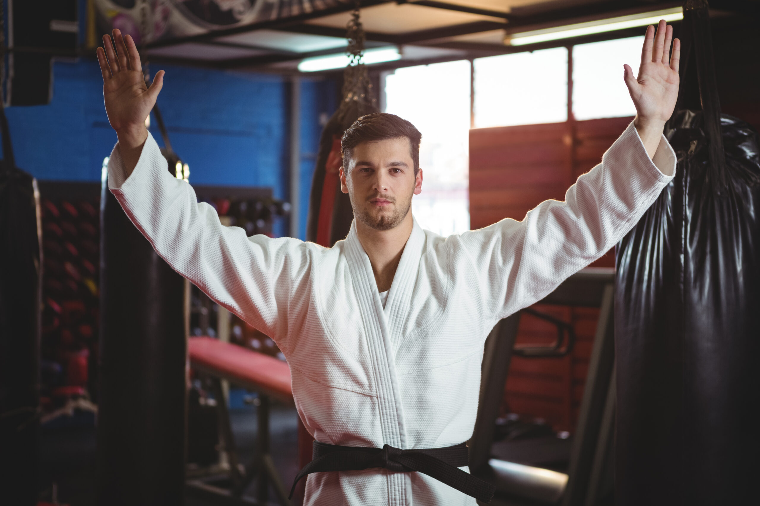 Karate player standing with arms spread in fitness studio Martial artist in uniform raising hands confidently in a dojo.
