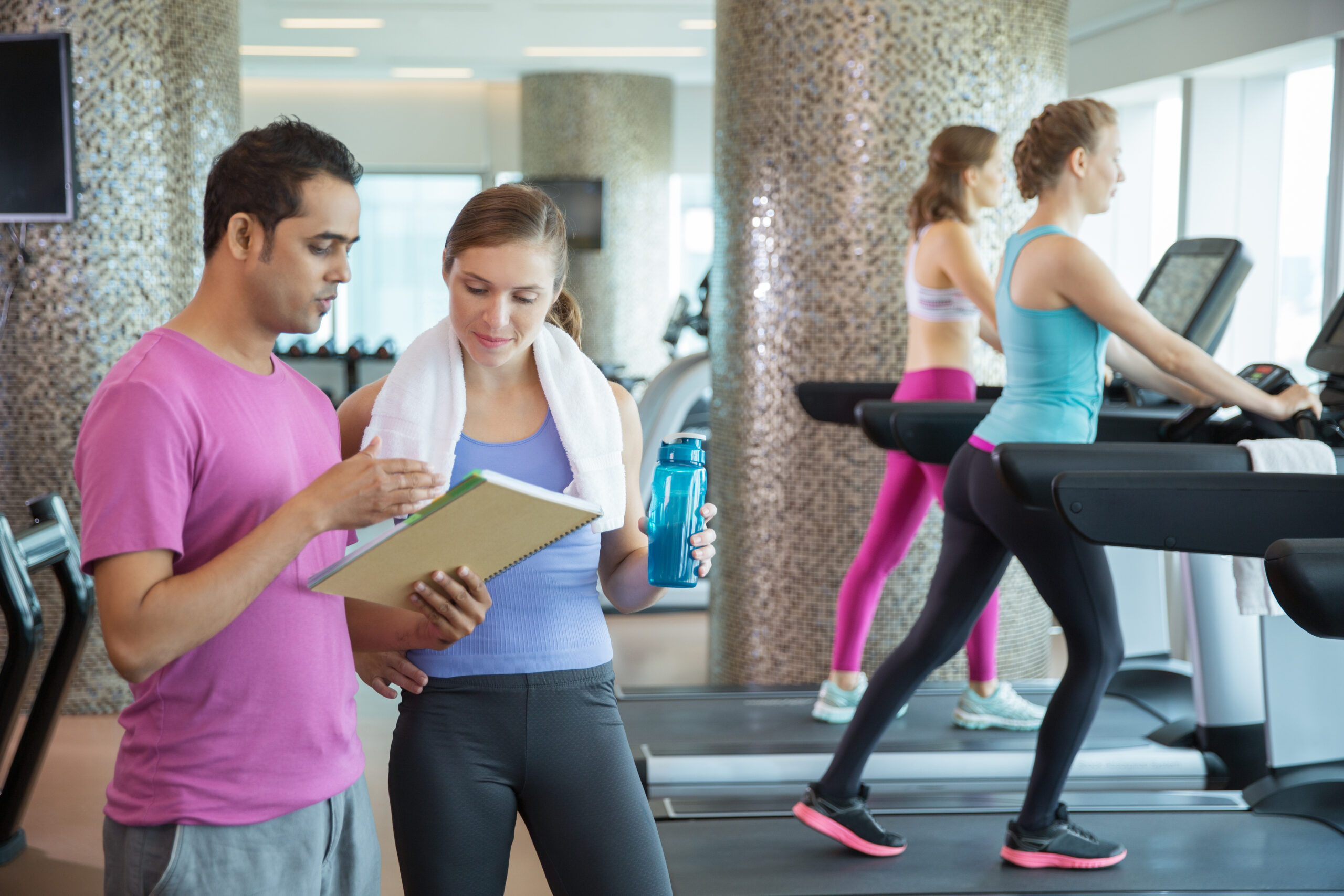 Sporty Young Woman Talking to Male Trainer in Gym A Trainer Discussing the Member Tracking Details