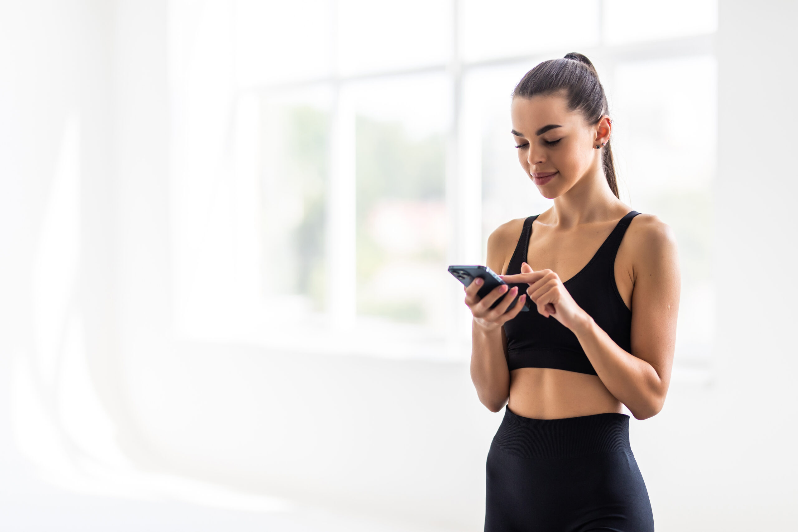 Attractive healthy young woman with a fitness mat using mobile phone at the gym Women making gym payment using her phone