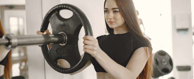 Young woman lifting a barbell with a weight plate in a gym