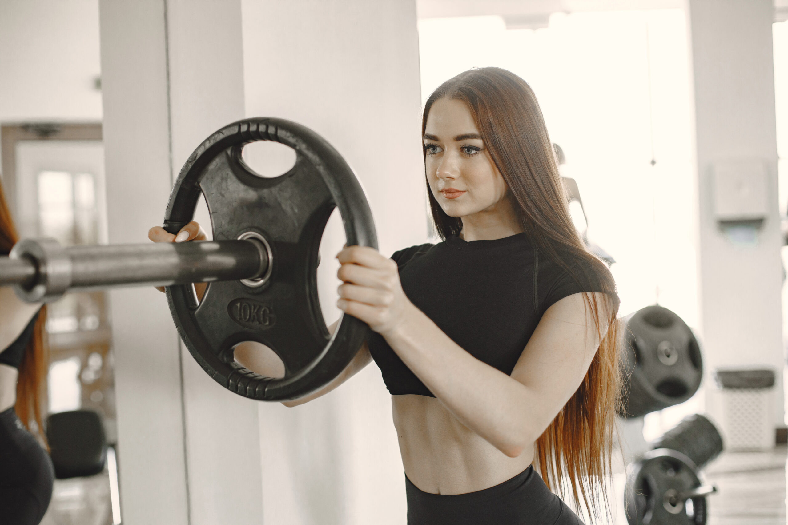 Young woman lifting a barbell with a weight plate in a gym