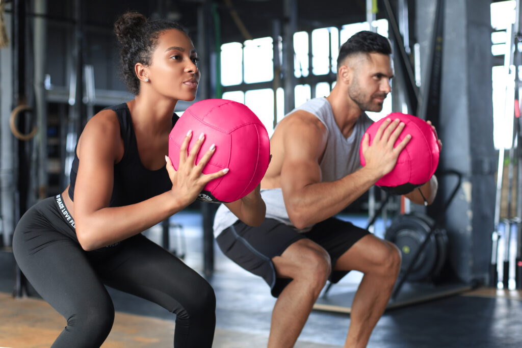 Athletes competing in a HYROX training session with wall balls in a gym setting.