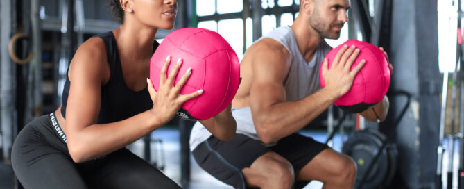 Athletes competing in a HYROX training session with wall balls in a gym setting.