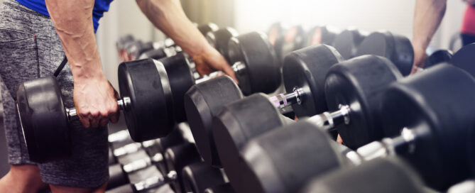 Man selecting dumbbells from a rack for weight training at the gym