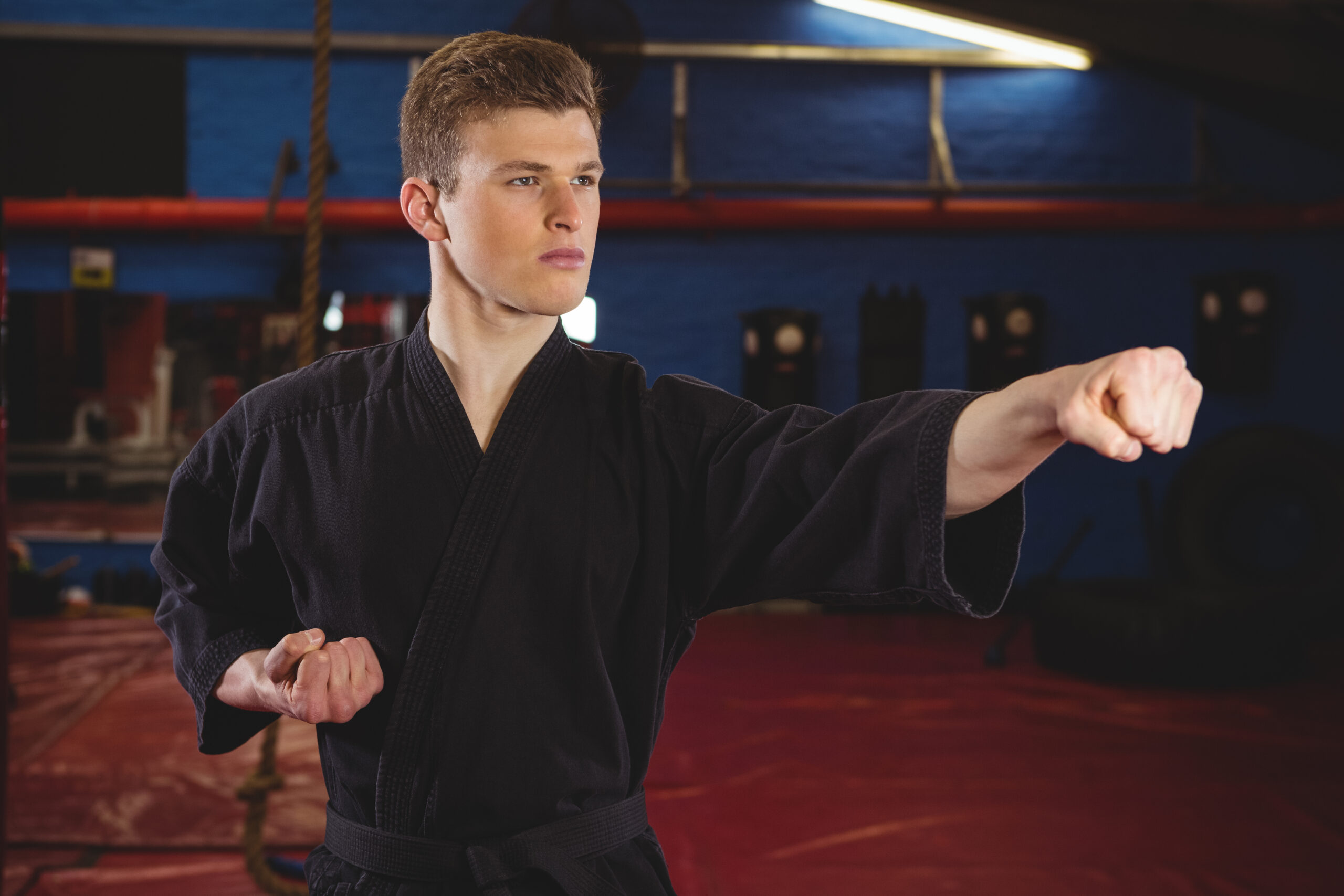 Karate player performing karate stance in fitness studio Man in a black martial arts uniform performs a straight punch in a gym, focused on technique during training.