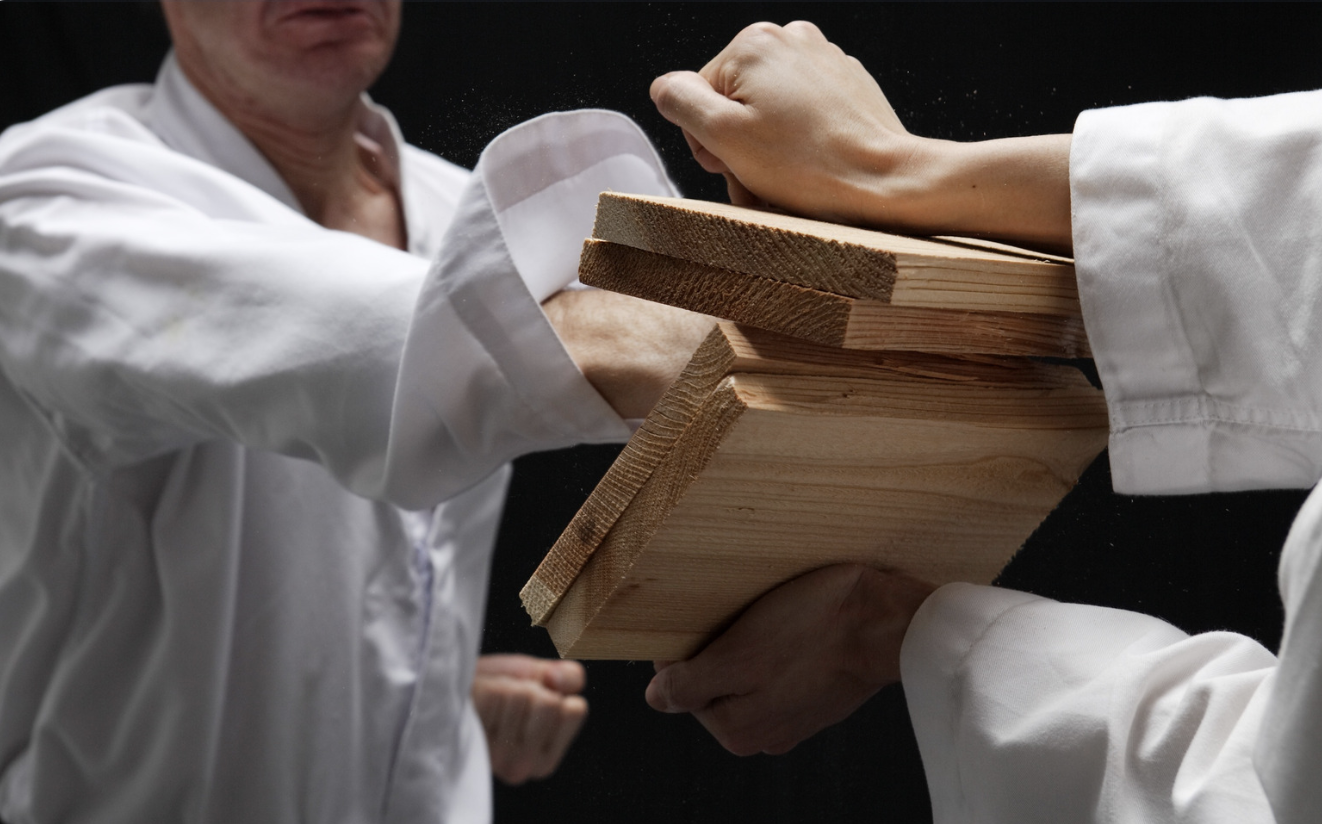 Image 14-06-26 at 7.42 PM Martial arts practitioner breaking a stack of wooden boards during a striking demonstration while an instructor observes the technique.