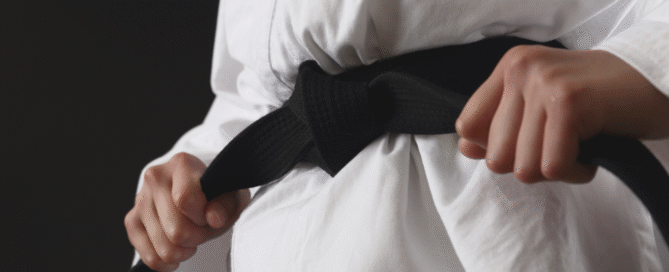 Close-up of a martial arts student tightening a black belt around a white gi.