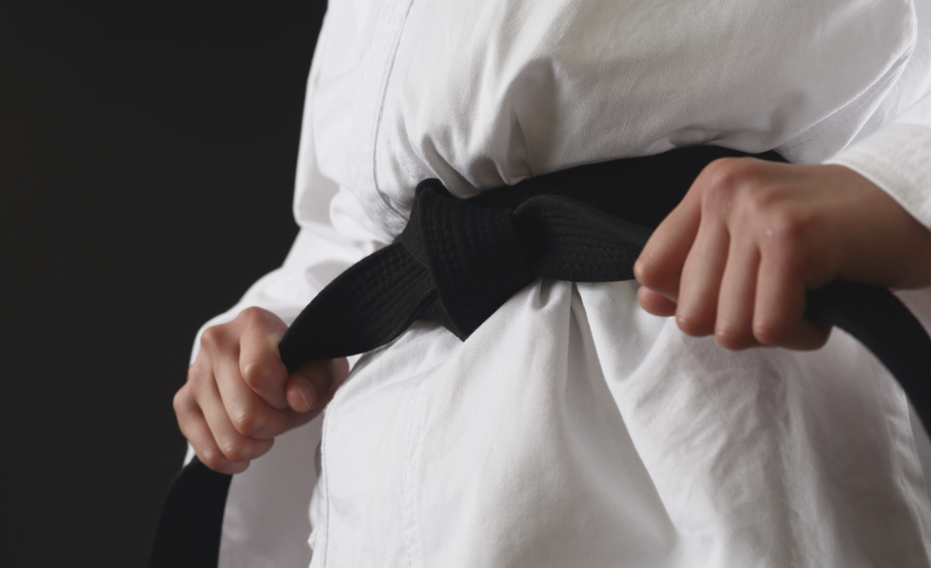 Close-up of a martial arts student tightening a black belt around a white gi.