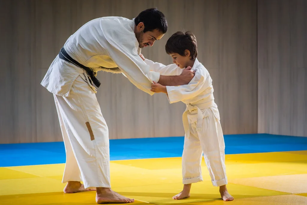 Martial arts instructor teaching a young student basic grappling techniques during a beginner class on training mats.