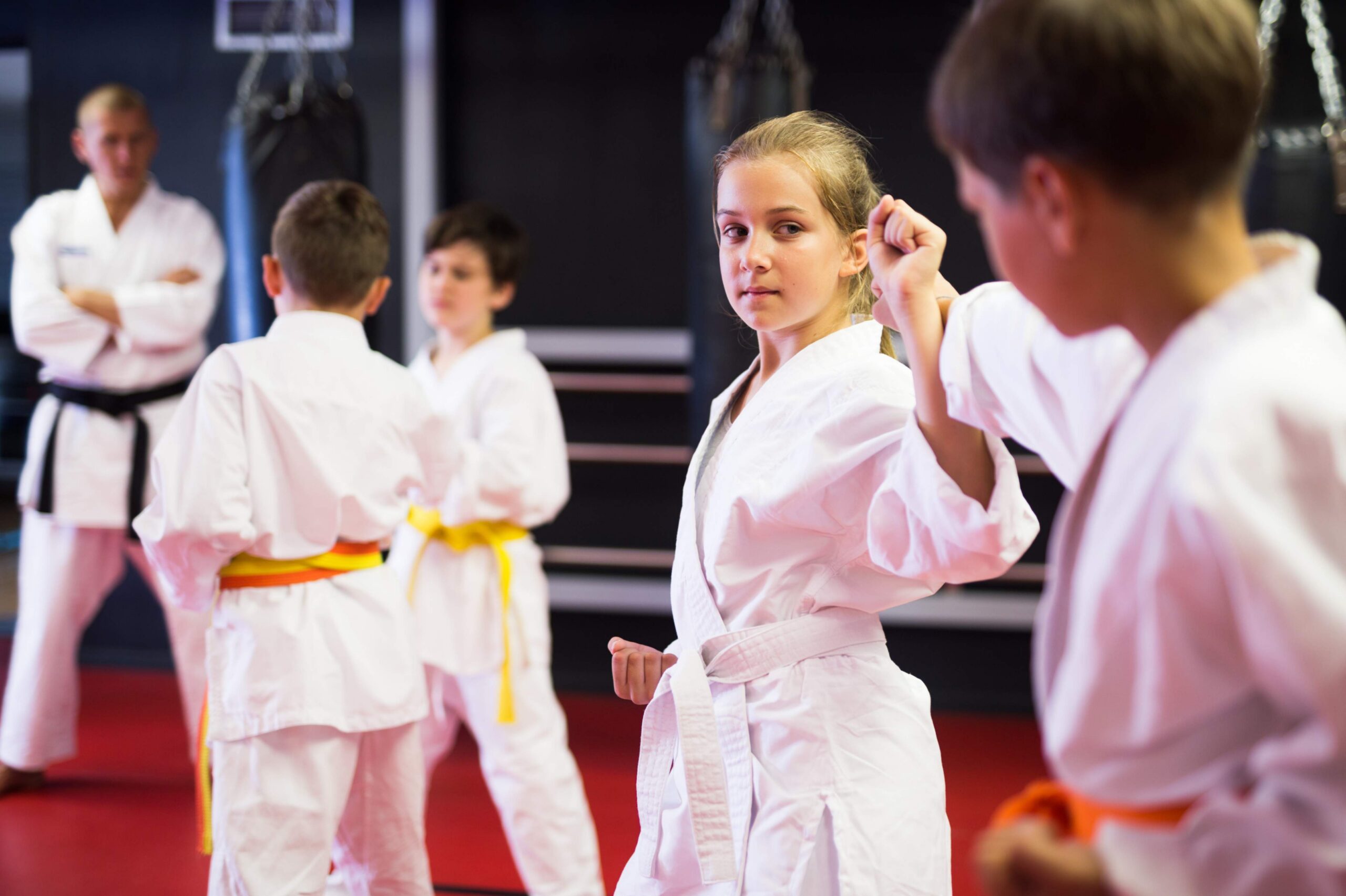 jpeg-optimizer_Diligent positive schoolchilds practicing new karate moves in pairs in class with trainer Young taekwondo students practice blocking techniques during a class while an instructor supervises in the background.