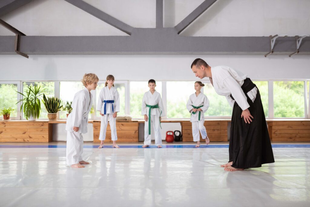 jpeg-optimizer_Cute blonde-haired boy greeting trainer before having a fight Martial arts instructor and young student bow to each other during a children's training class in a dojo.
